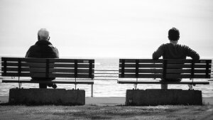 Alter und junger Mann sitzen auf einer Bank und sehen auf das Meer